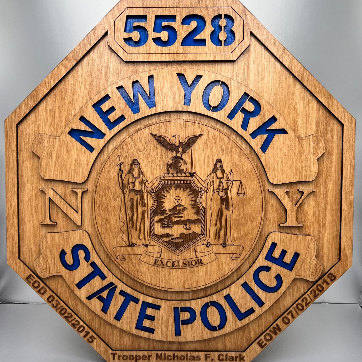 A laser engraved wooden replica of a New York State Police shield badge with a blue background for the text.